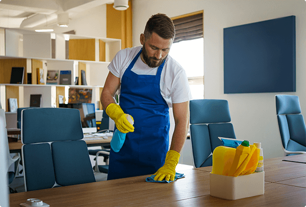 Man wearing apron and gloves wiping table.
